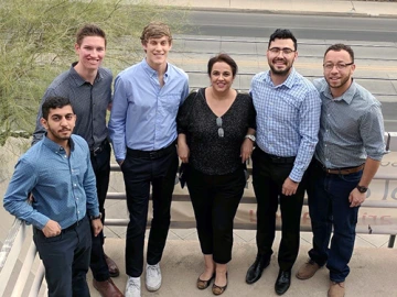 Five men and one woman smiling and posing in a group outside