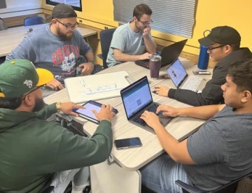 five students at a table working on computers