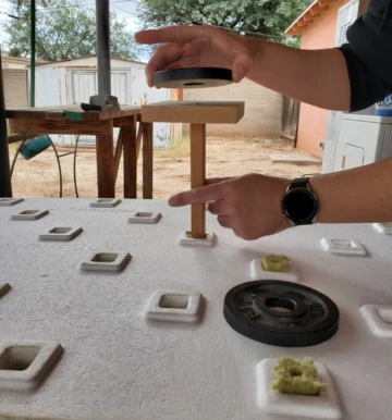 a foam board with square holes in it. a pair of hands is setting a weight on top of a stick that fits into one of the holes.