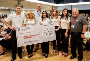 seven people stand indoors with a large check