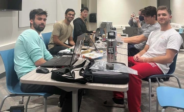 a group of six students works on computers at a table