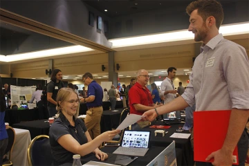 Image of Optical sciences and engineering senior Evan Mekenney, right, hands his resume to Lisa Bennett, a mechanical engineer at GEOST and UA alumna.