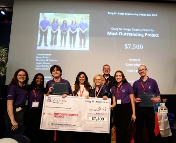 A group of 7 people poses with a large prize check