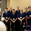 Six men and one women pose for a photo next to a robot with a golf club.