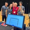 Five students in gray shirts take a photo with an older man.