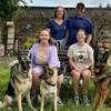 A man in a blue shirt takes a photo with his wife and two daughters. They also have three German shepherds.