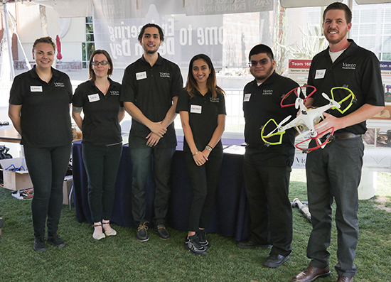 Three female and three male students standing under a tent outdoors holding a drone