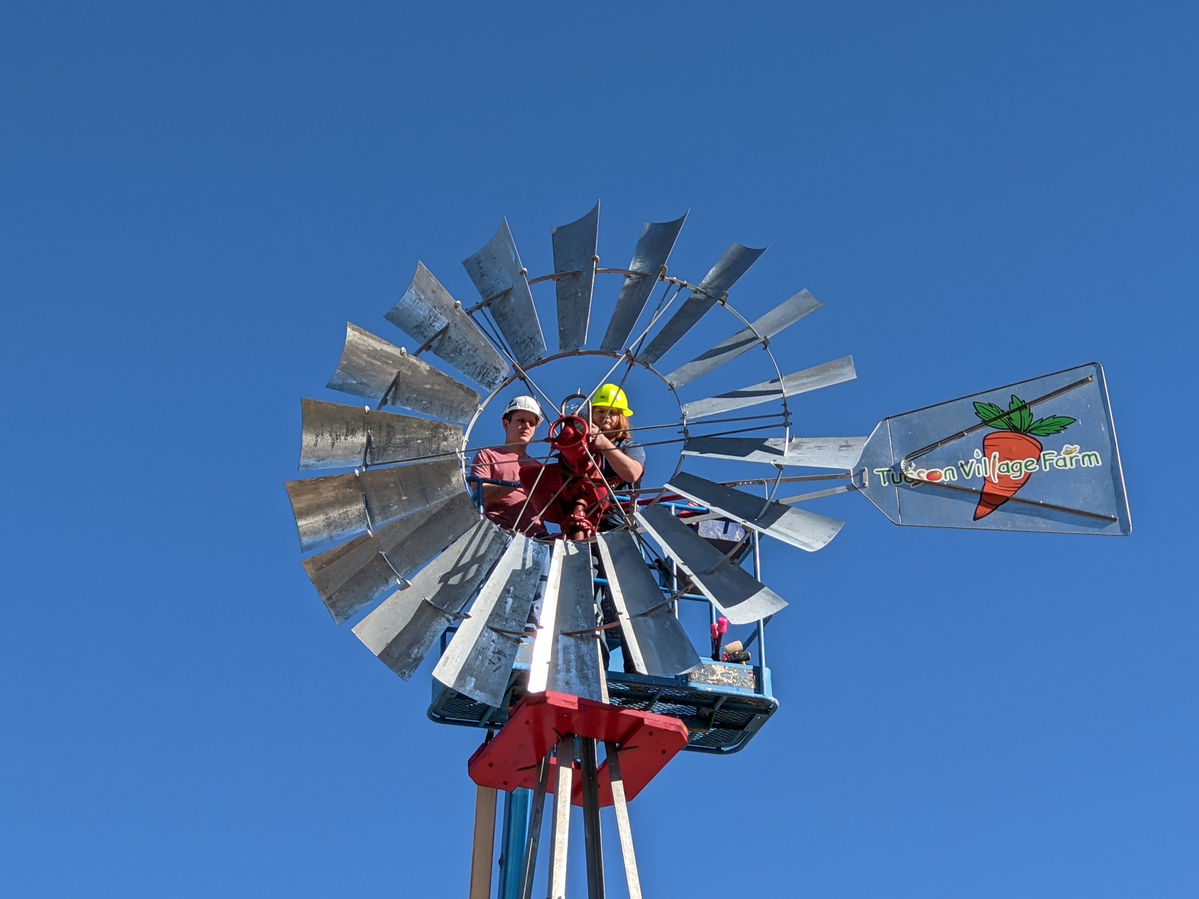 Two students look at the camera through the center of a decorative windmill. Behind them is a blue sky