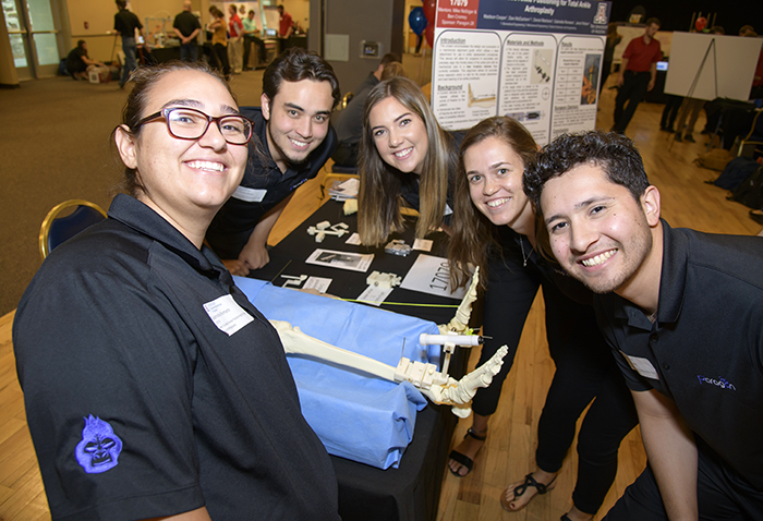Five students smiling around a skeletal leg model