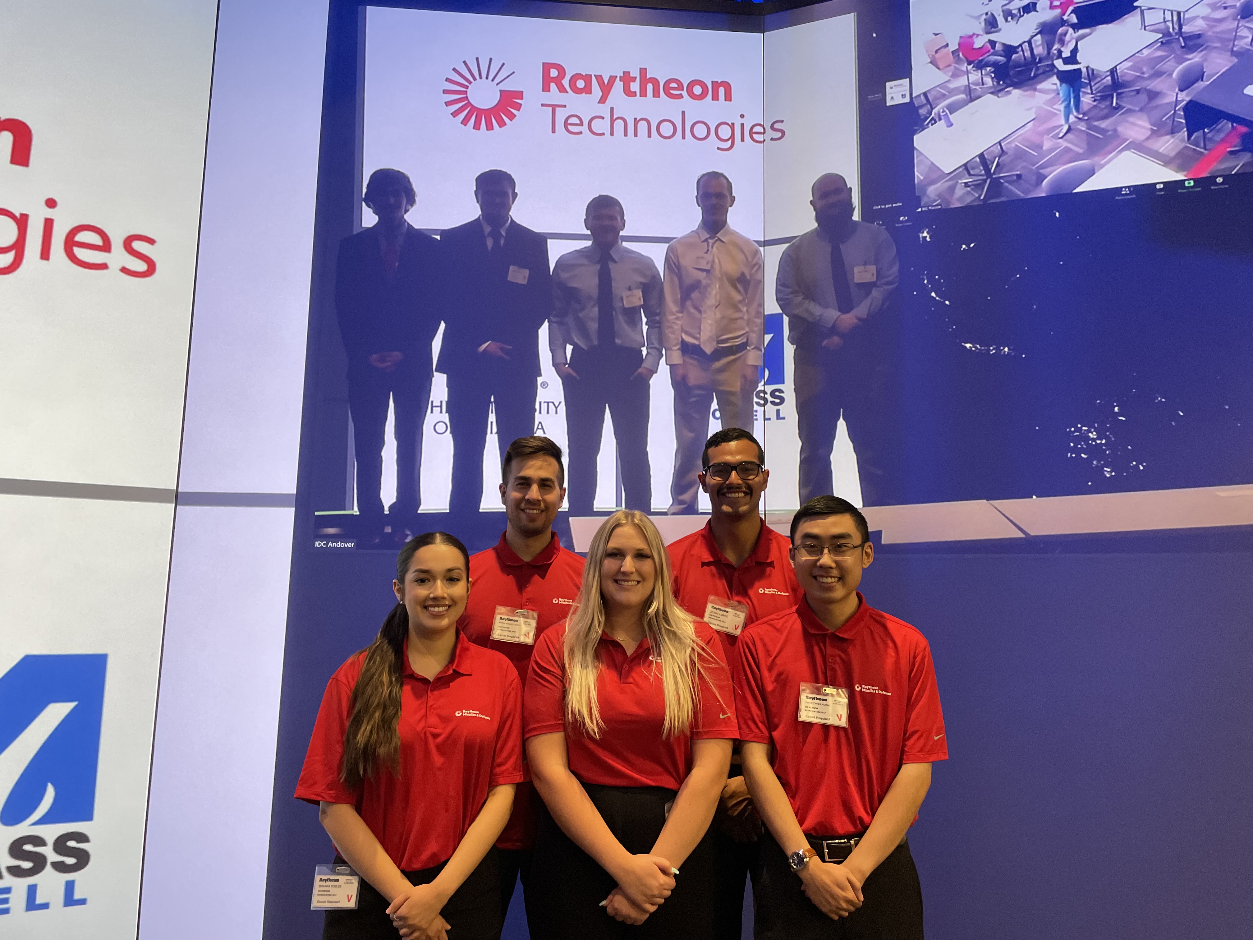 five students stand in front of a screen at a hybrid presentation meeting
