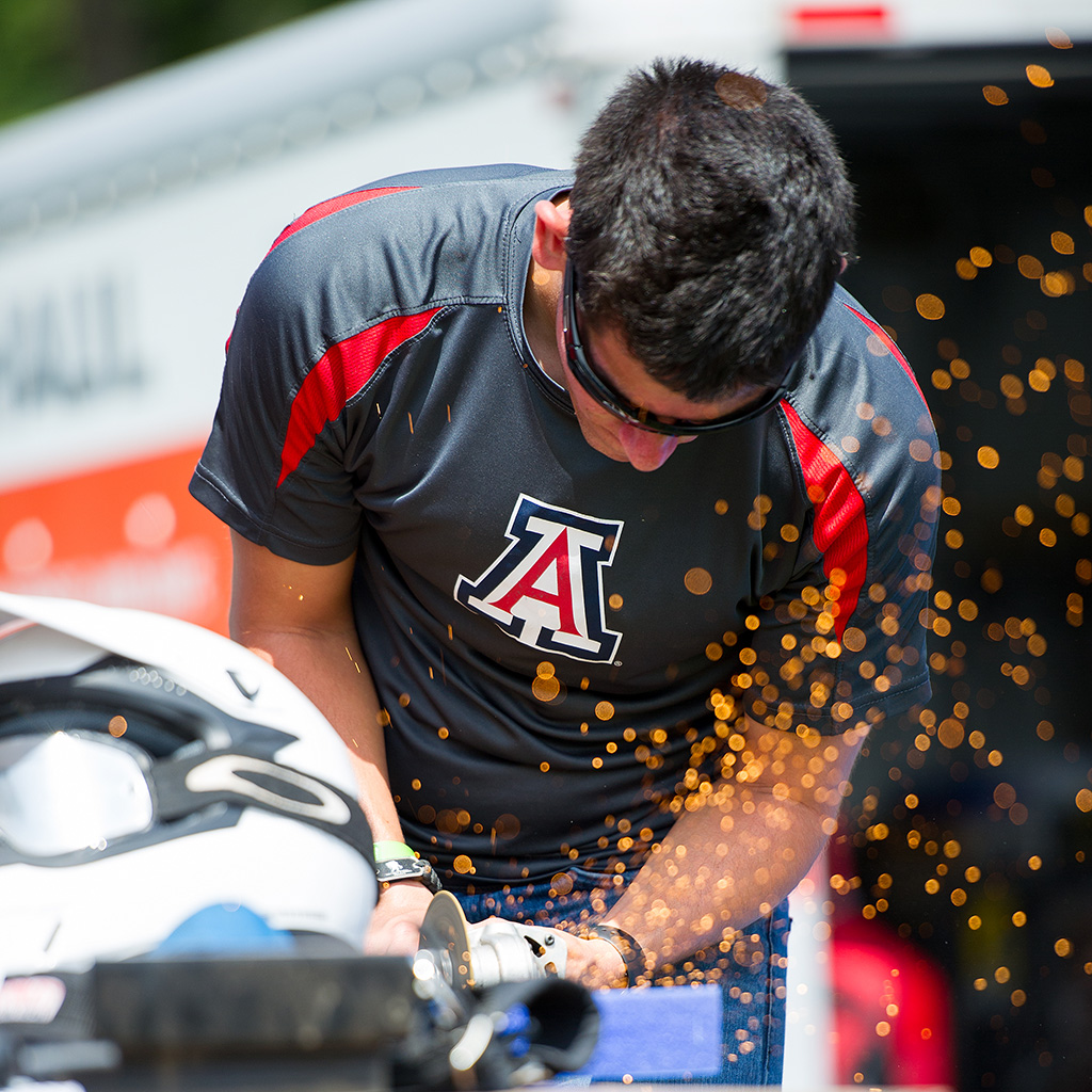 Student wearing UA shirt and protective eyewear uses a circular saw to cut metal, sending up a shower of sparks