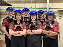 Six students pose indoors wearing welding helmes