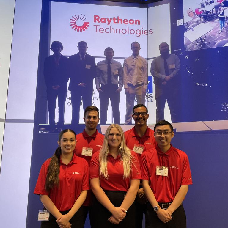 five students stand in front of a screen at a hybrid presentation meeting