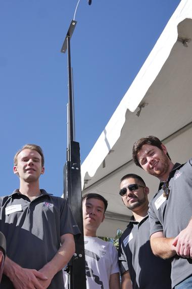 Four male university students standing outside next to a tall antenna mast
