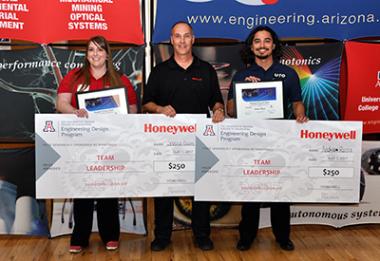 Two university students being awarded large prize checks by a man