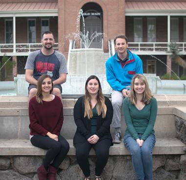 Two men and three women posing in front of a fountain outside of Old Main at the University of Arizona