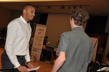 A man representing a company speaks to a university student at an open house