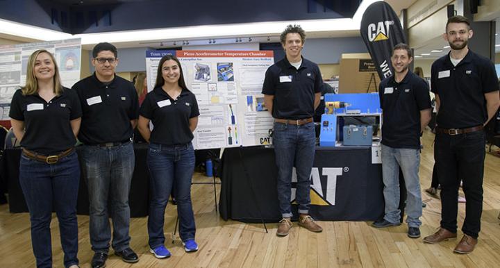 Six students stand in front of the poster that details their piezoaccelerometer temperature chamber