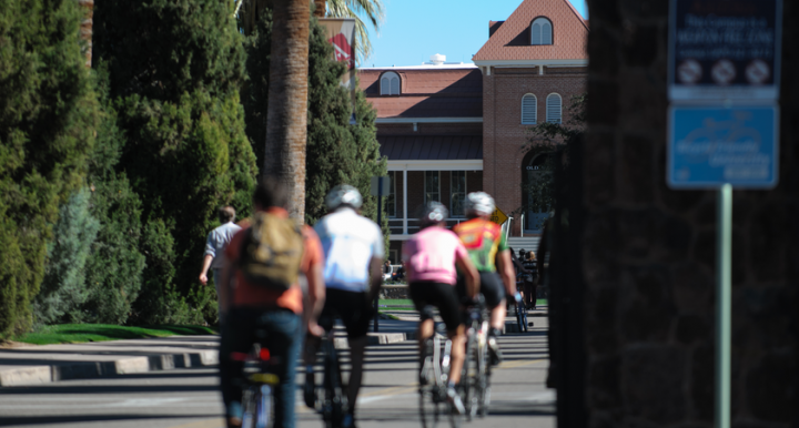 several people ride bicycles on the University of Arizona campus near Old Main