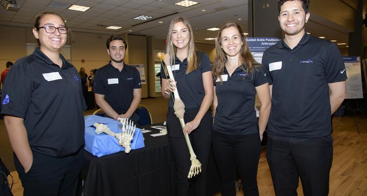 Five students on an engineering design team in a ballroom holding a skeletal leg