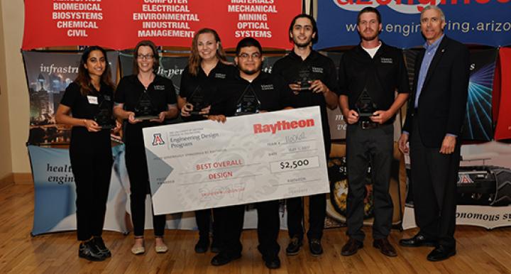 Sponsor with six university students holding triangle-shaped glass awards and a large award check 