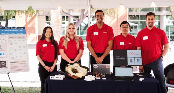 five students standing outside with a conference display
