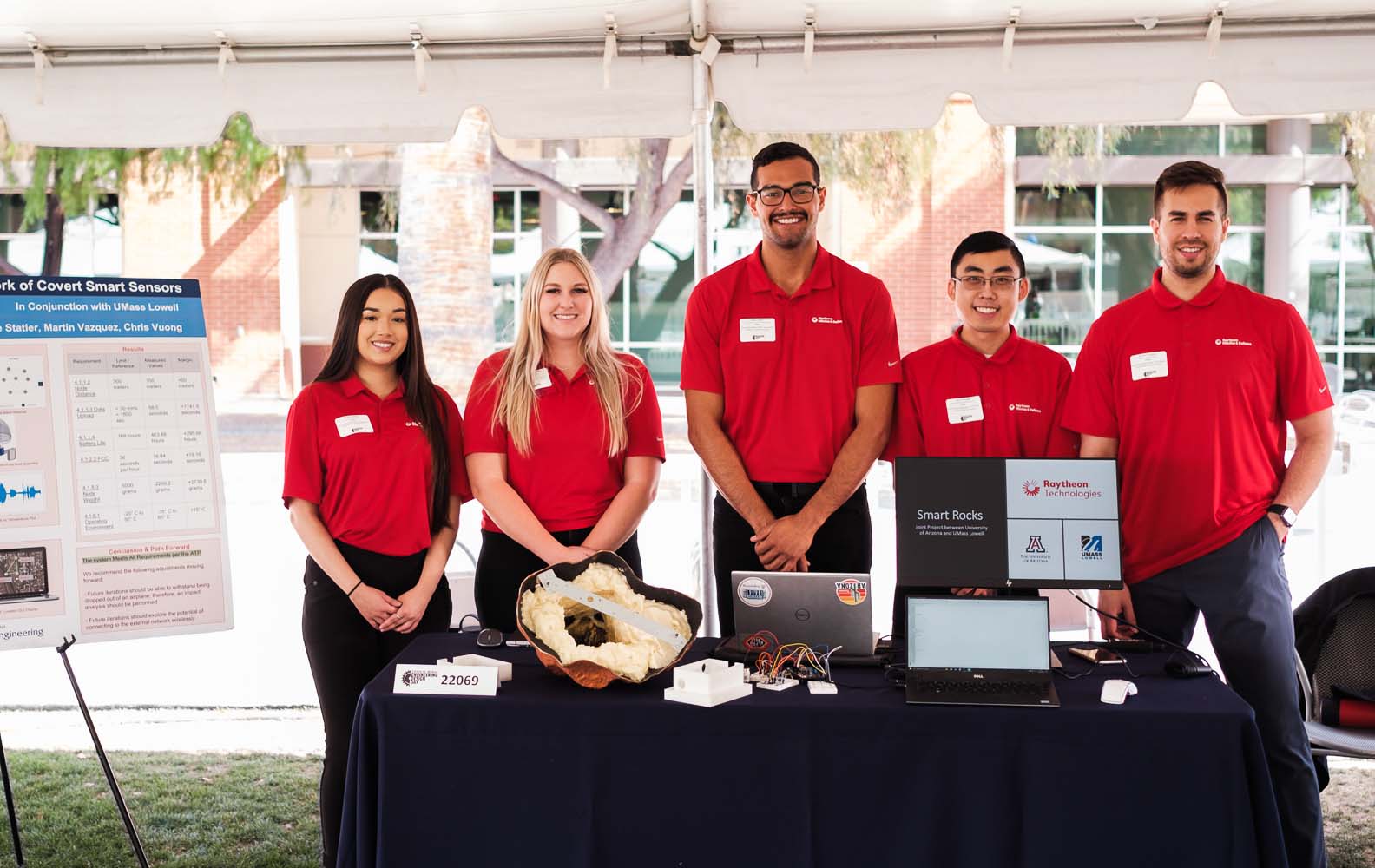 five students standing outside with a conference display